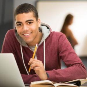 smiling student at table with laptop & books holding pencil